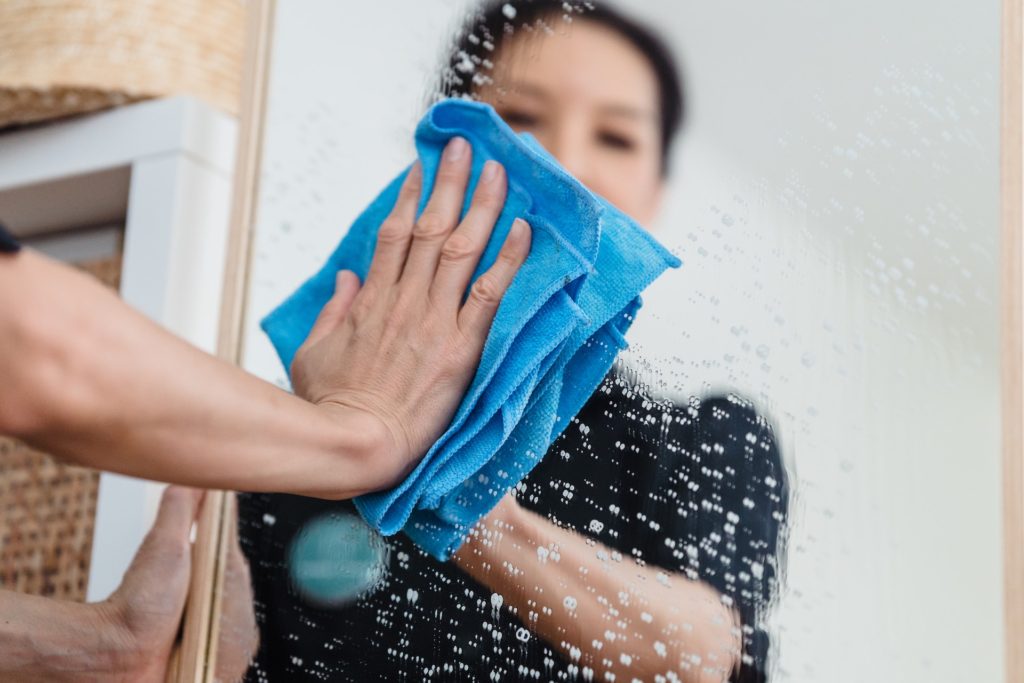 woman cleaning mirror with microfiber towel