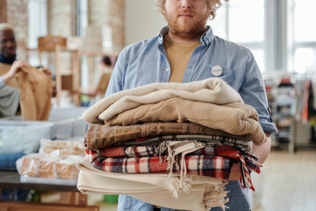 volunteer holding stack of donated clothes in thrift store